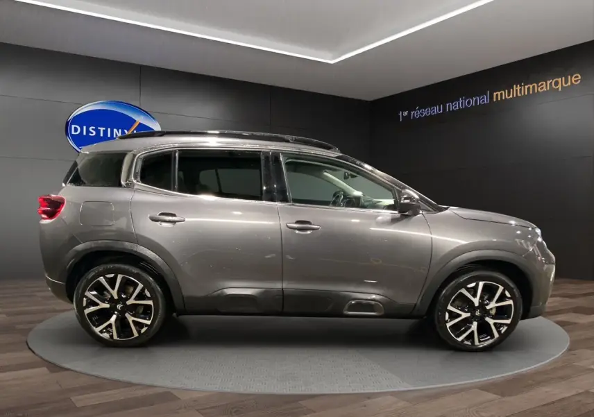 Profil droit d'un SUV Citroën C5 Aircross gris platinium avec jantes alliage noires et toit panoramique en showroom.