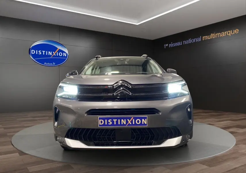 Vue frontale d'un Citroën C5 Aircross gris platinium 2023 avec phares LED allumés en showroom.
