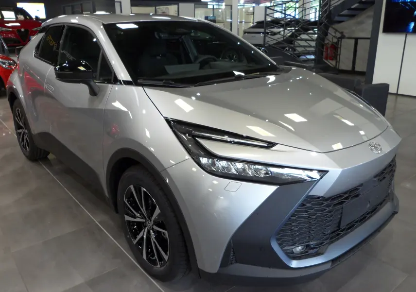 Toyota C-HR hybride 140 ch style gris minéral en 3/4 avant droit, avec jantes biton et calandre imposante.