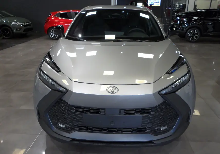 Vue frontale d'un Toyota C-HR hybride gris minéral avec calandre large noire et phares effilés en showroom.