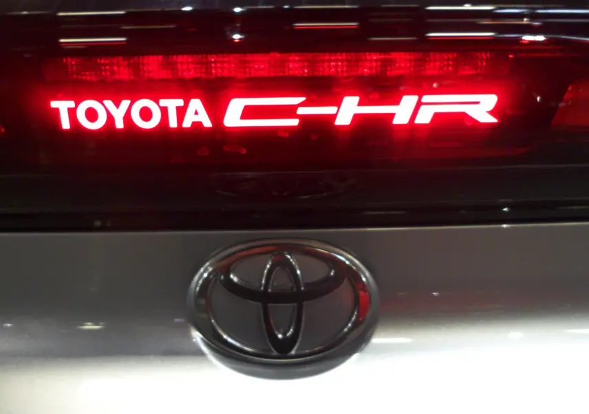 Gros plan sur le logo Toyota et l'inscription lumineuse C-HR rouge sur la malle arrière gris minéral du véhicule.