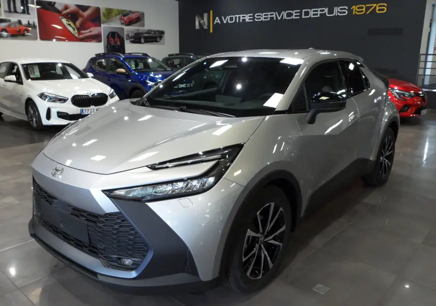 Toyota C-HR hybride gris minéral vu en 3/4 avant droit dans un showroom avec jantes bi-ton noires.