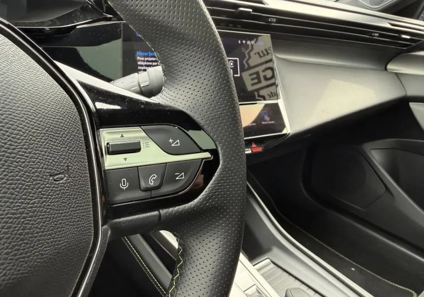 Gros plan sur le volant noir perforé avec commandes intégrées et tableau de bord moderne du Peugeot 408 blanc 2024