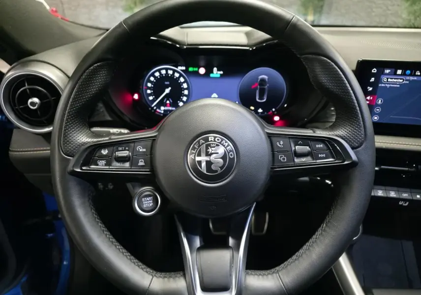 Vue frontale du volant en cuir noir de l'Alfa Romeo Tonale 2025, avec tableau de bord digital et bouton start/stop visible.