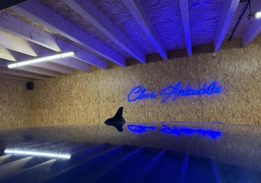 Vue rapprochée du toit bleu brillant d’un Volkswagen T-Roc 2019 avec antenne requin, reflet d’un néon bleu en arrière-plan.