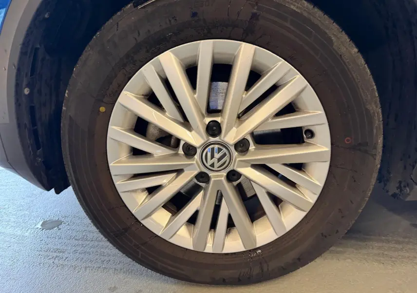 Gros plan sur la jante alliage argentée avec logo Volkswagen au centre, montée sur un pneu noir du T-Roc bleu.