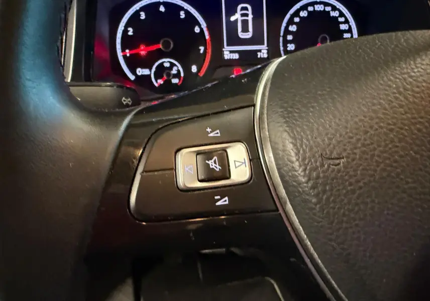 Gros plan sur le volant cuir et commandes audio du Volkswagen T-Roc 1.0 TSI 115 Lounge, tableau de bord éclairé en arrière-plan.