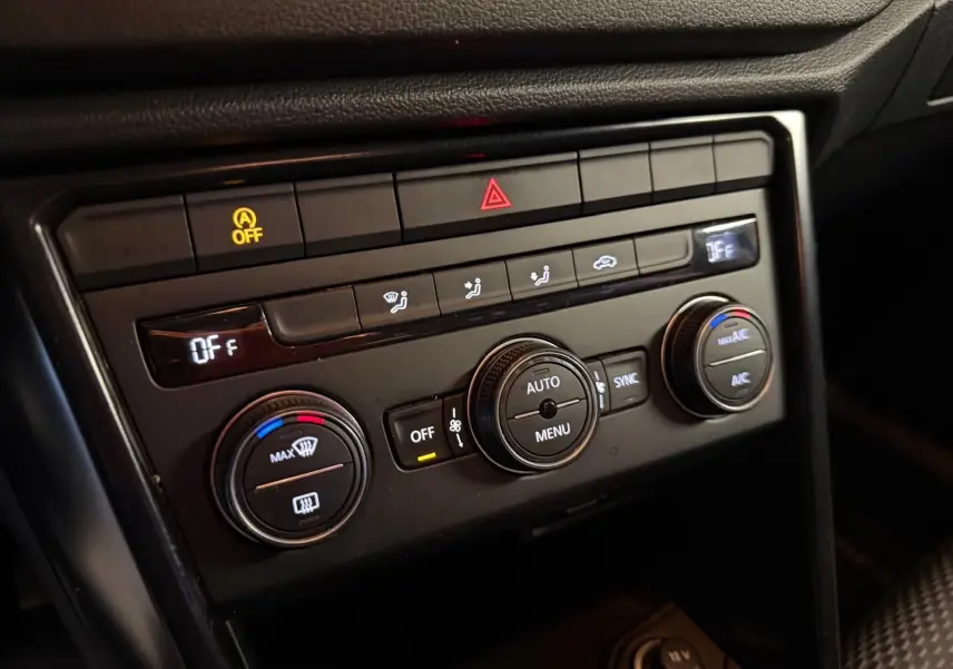 Vue rapprochée de la console de climatisation noire du Volkswagen T-Roc 1.0 TSI 115 Lounge avec commandes rotatives et affichage digital.