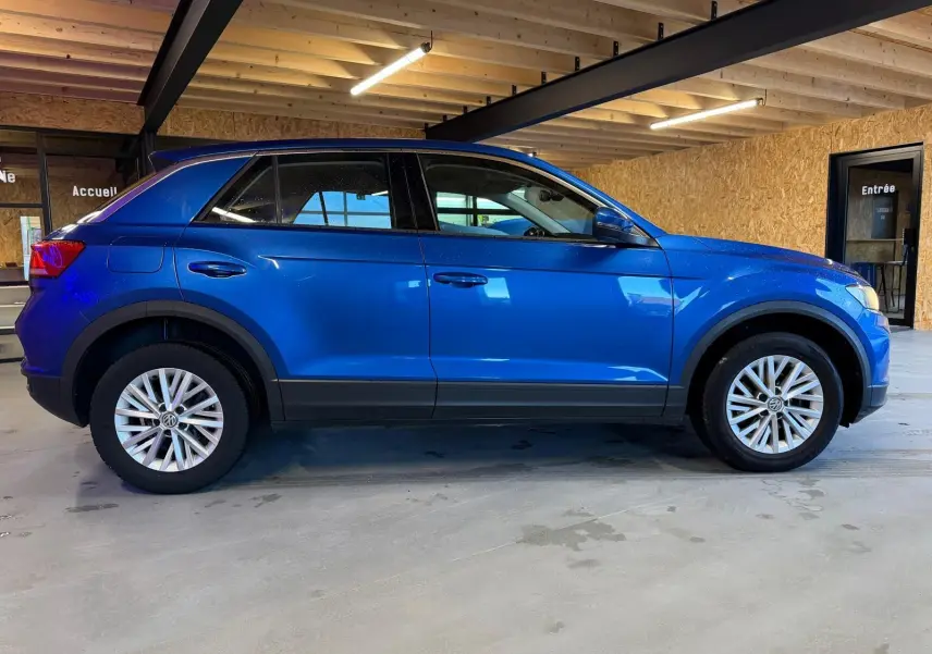 Vue de profil côté gauche d'un Volkswagen T-Roc bleu 2019 avec jantes alliage et rétroviseurs électriques rabattables.