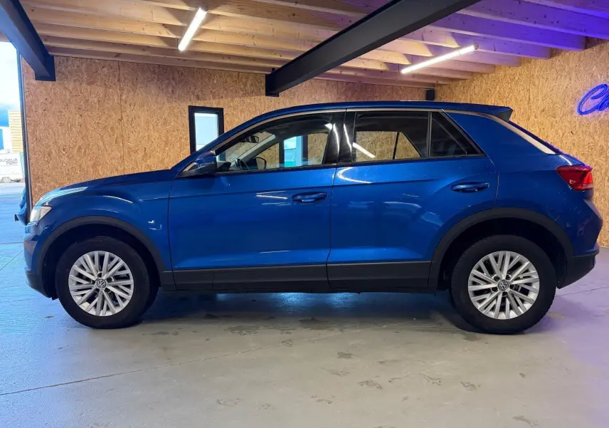 Vue latérale droite d'un Volkswagen T-Roc bleu 2019 avec jantes alliage et vitres teintées en intérieur d'atelier.