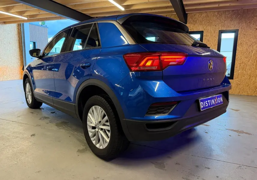 Vue 3/4 arrière droite du Volkswagen T-Roc bleu 2019 avec feux arrière allumés et jantes argentées.