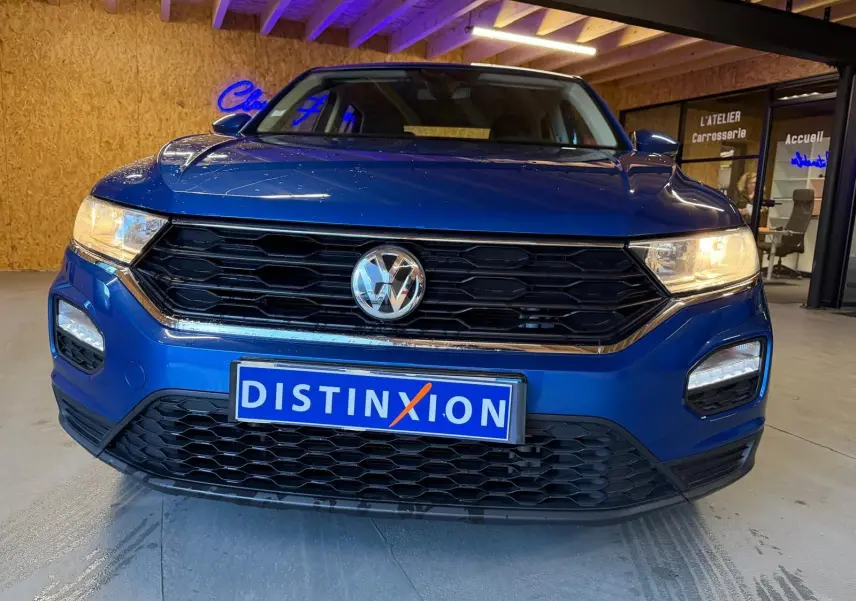 Vue avant d'un Volkswagen T-Roc bleu 2019 avec calandre noire et feux allumés en intérieur.