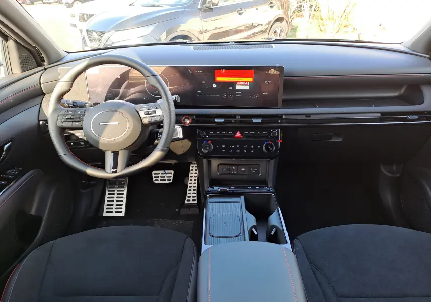 Vue intérieure frontale du Hyundai Tucson 2025, tableau de bord noir avec écran large et volant multifonction en cuir.