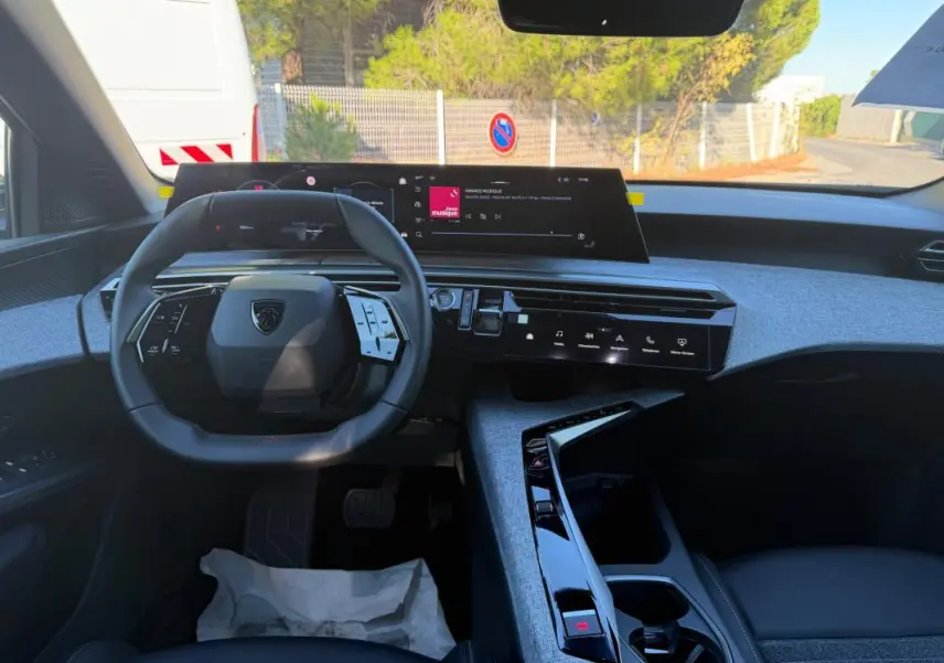 Vue intérieure du tableau de bord et volant du Peugeot 3008 Hybrid 145 e-DCS6 Allure 2025 avec finition tissu bleu et écrans numériques.