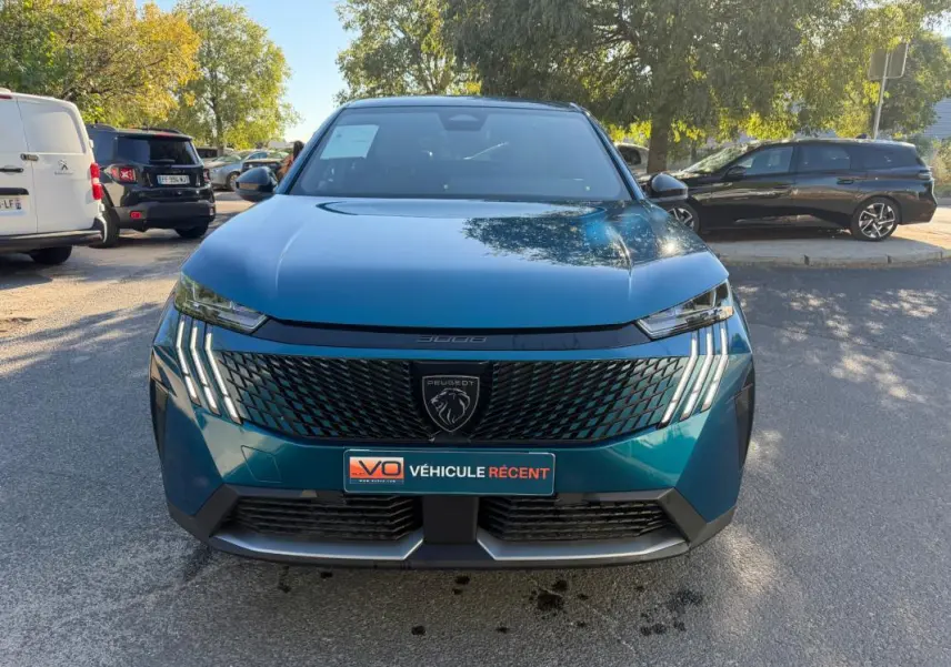 Vue frontale d’un Peugeot 3008 Hybrid bleu 2025 avec calandre noire et feux LED distinctifs allumés.