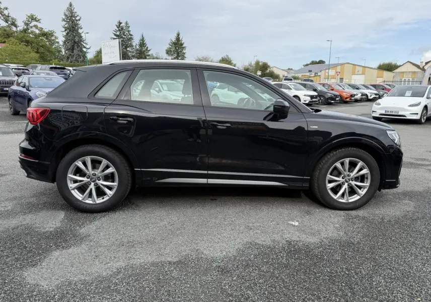 Audi Q3 S Line noire vue de profil côté gauche sur un parking avec jantes en aluminium et vitres légèrement teintées.