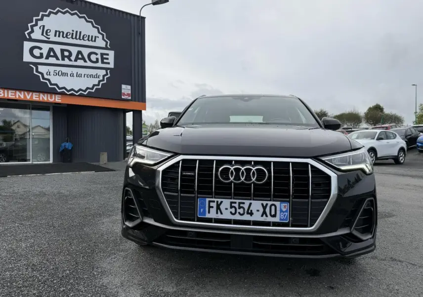 Audi Q3 Quattro S Line noire vue de face avec calandre chromée et phares LED allumés sur parking devant garage.