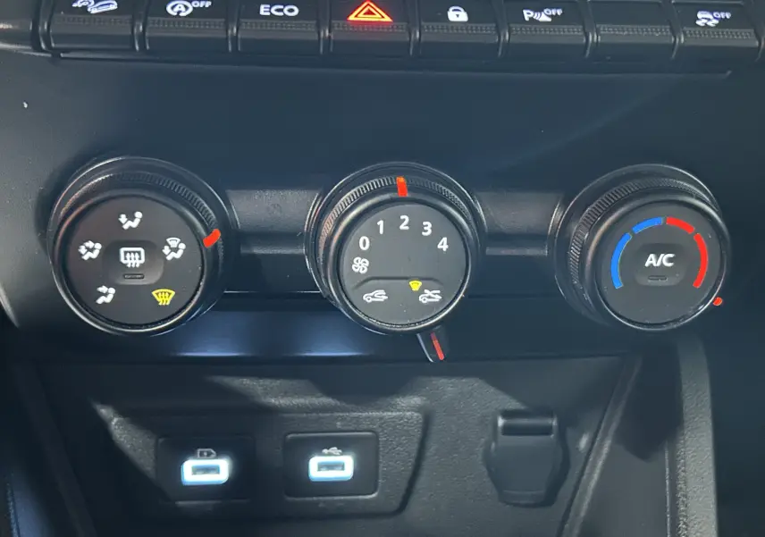 Gros plan sur les commandes de climatisation et les ports USB du tableau de bord du Dacia Duster blanc 2023.
