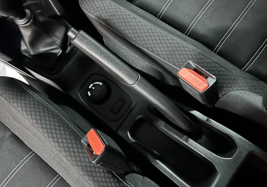 Vue rapprochée de la console centrale du Dacia Duster 2023, montrant frein à main et sièges tissu noirs avec surpiqûres blanches.