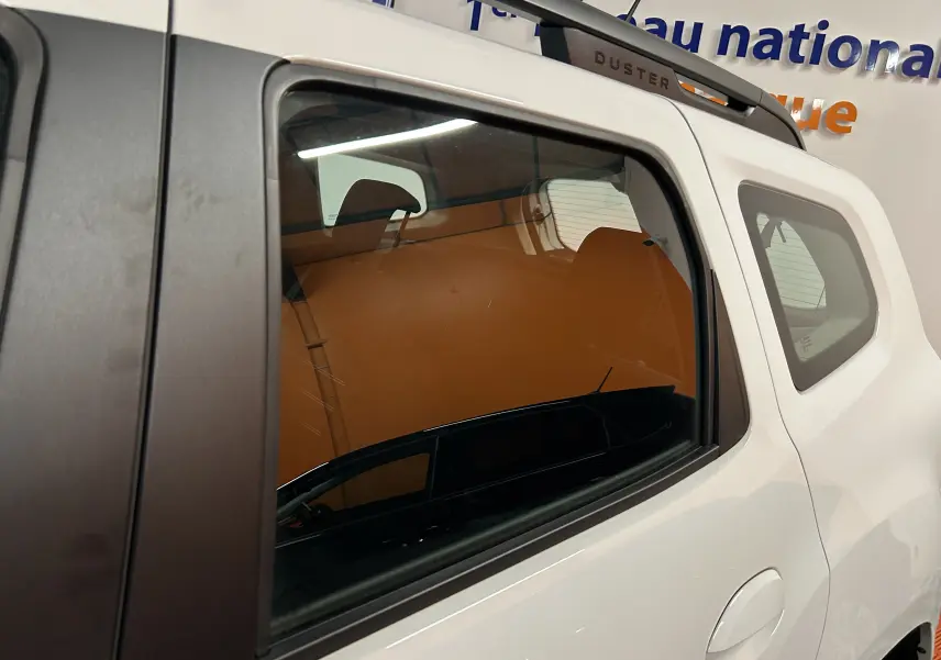 Vue latérale droite sur la porte arrière blanche du Dacia Duster 2023 avec toit ouvrant et logo Duster sur le montant.
