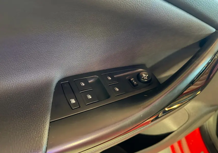 Gros plan sur les commandes de vitres et rétroviseurs côté conducteur d'une Opel Astra rouge.