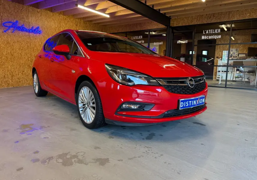 Opel Astra rouge vue 3/4 avant droit dans un garage avec éclairage intérieur et enseigne néon bleue.