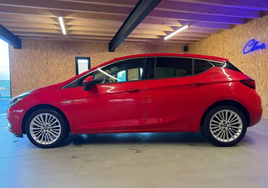 Opel Astra 1.4i Turbo rouge vue de profil côté gauche, avec jantes alu et rétroviseurs électriques rabattables.