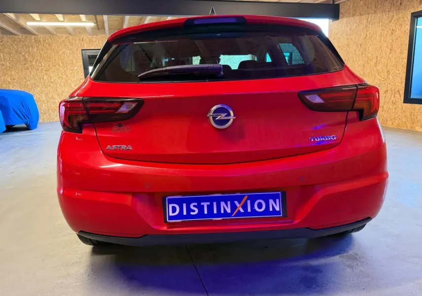 Vue arrière d'une Opel Astra rouge 2016 avec badges "Astra" et "Turbo" visibles, stationnée en intérieur.