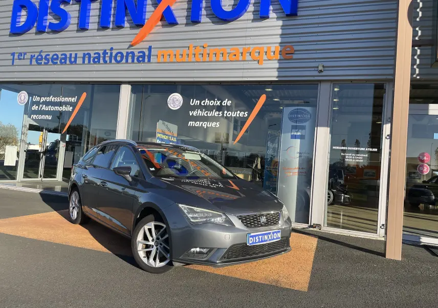 SEAT LEON ST gris en 3/4 avant droit, stationnée devant un showroom avec plaques Distinxion visibles.