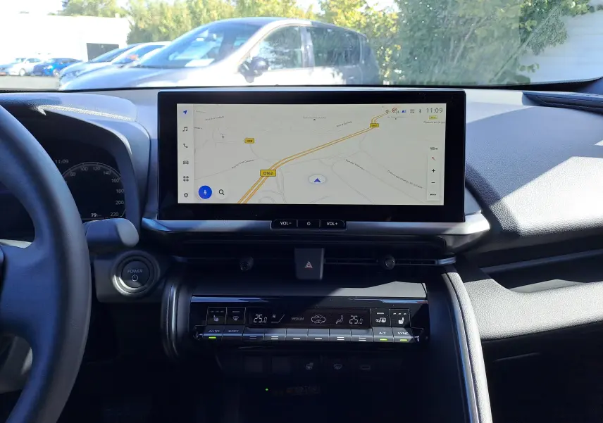 Vue intérieure du tableau de bord du Toyota C-HR gris minéral 2025, avec écran tactile de navigation et commandes climatisation.