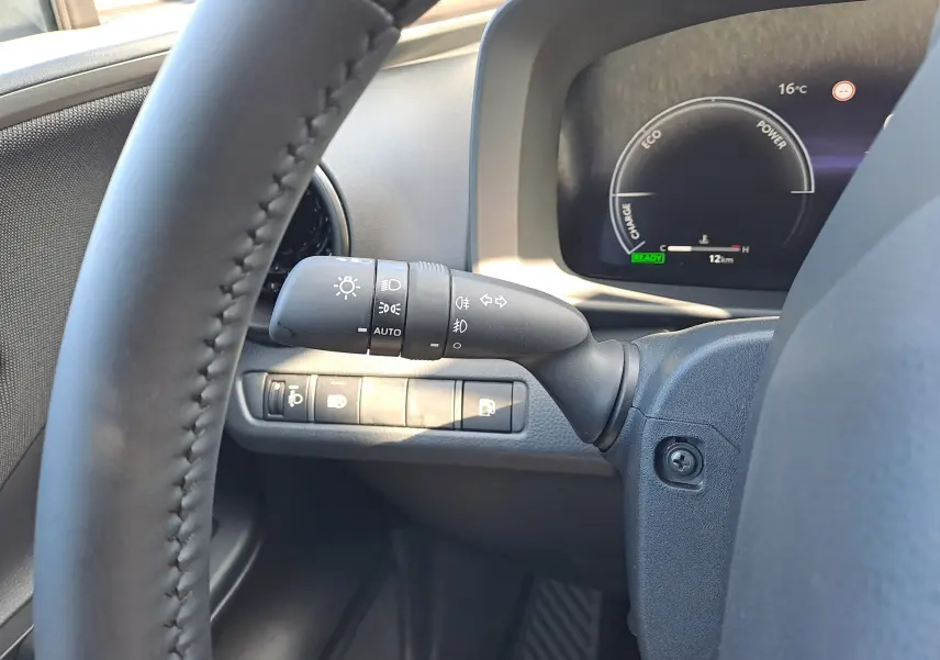 Gros plan sur la manette d'éclairage à gauche du volant du Toyota C-HR gris minéral, tableau de bord numérique visible.