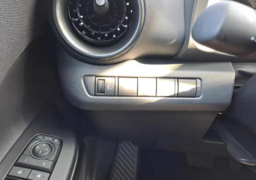 Détail intérieur côté gauche du tableau de bord noir du Toyota C-HR gris minéral 2025 avec commandes des rétroviseurs et ventilation.