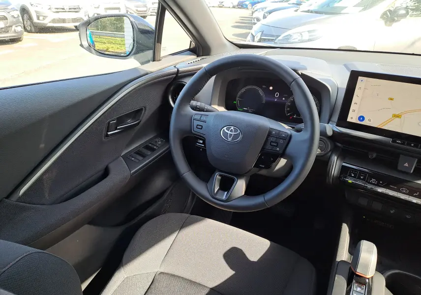 Vue intérieure côté conducteur du Toyota C-HR gris minéral 2025, avec volant multifonction et écran tactile de navigation.