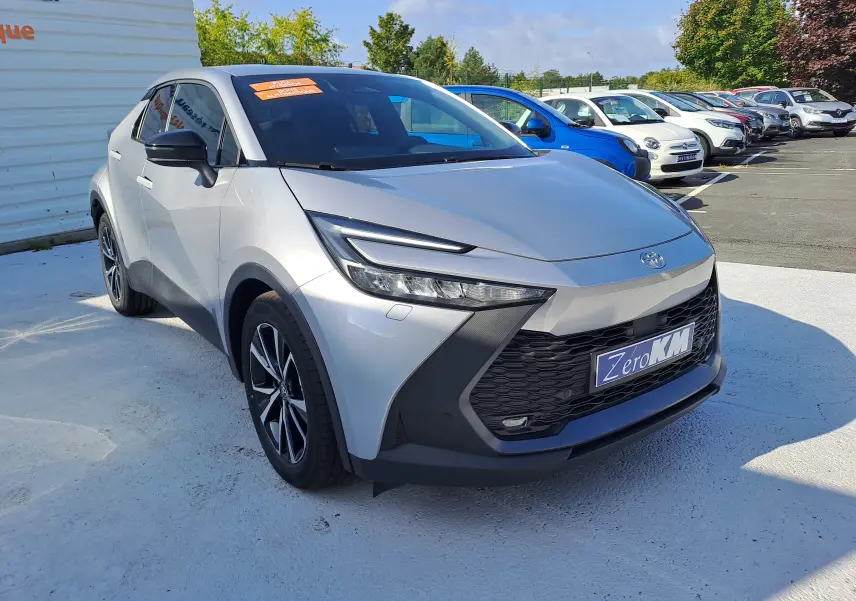Toyota C-HR II Style 1.8 Hybrid gris minéral vu en 3/4 avant droit, avec calandre noire et jantes biton 18 pouces.