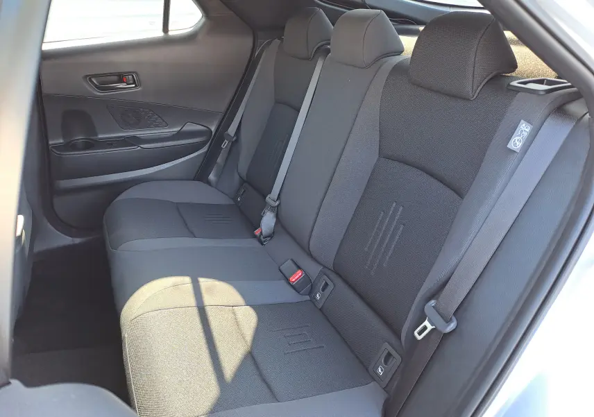 Vue intérieure sur la banquette arrière grise du Toyota C-HR II Style 1.8 Hybrid 2025, avec ceintures et appuie-têtes visibles.