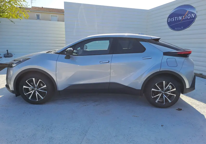 Profil côté gauche du Toyota C-HR 2025 gris minéral avec jantes biton et lignes sculptées distinctives.