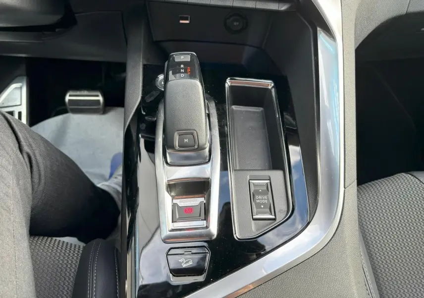 Vue plongeante sur la console centrale noire brillante du Peugeot 3008 2024, avec levier de vitesses automatique et bouton Drive Mode.