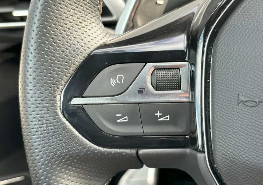 Gros plan sur les commandes gauche du volant cuir perforé du Peugeot 3008 2024 blanc nacré avec touches chromées.