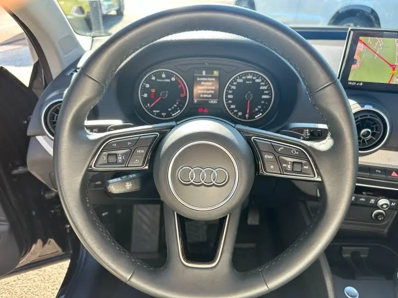 Vue rapprochée du volant cuir noir de l'Audi Q2 35 TFSI S line 2023 avec tableau de bord et écran GPS visibles.
