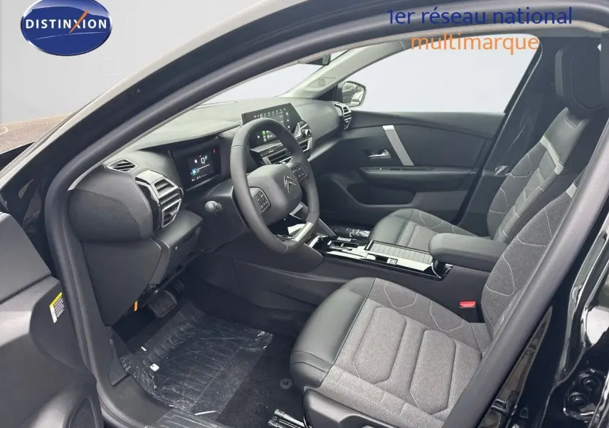 Intérieur avant droit d'une Citroën C4 noire métal 2024, sièges tissu et cuir gris, tableau de bord moderne avec écran tactile.