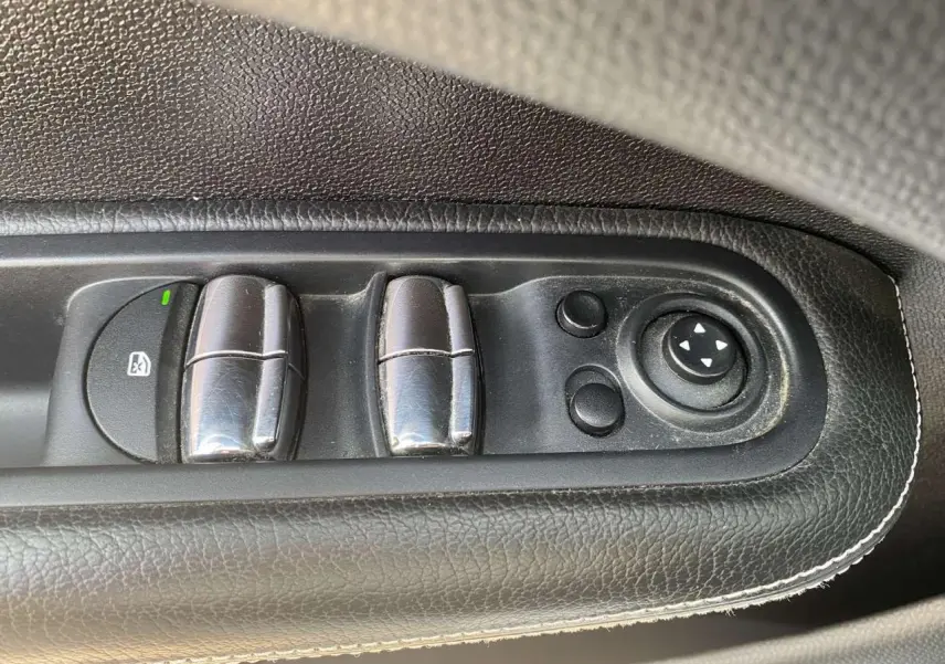 Gros plan sur les commandes des lève-vitres et réglages des rétroviseurs côté conducteur en cuir noir du MINI Countryman gris clair.