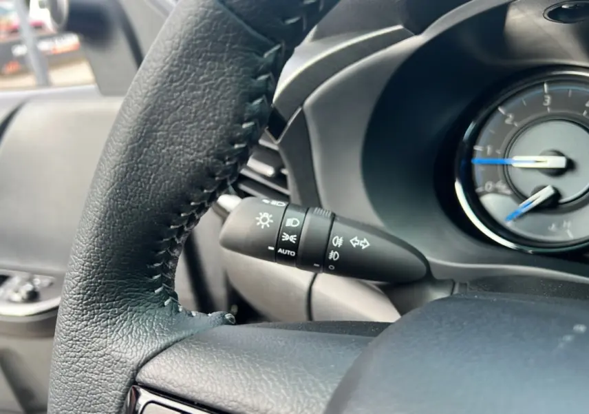 Gros plan sur le volant et la manette des feux du Toyota Hilux 2025 gris atlas, tableau de bord partiel visible.