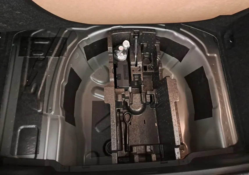 Vue plongeante sur le coffre ouvert du Skoda Kamiq gris graphite, montrant le rangement pour roue de secours et outils intégrés.