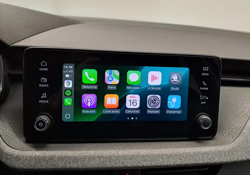 Écran tactile central du Skoda Kamiq 2025 affichant des applications connectées, entouré de commandes noires sur tableau de bord gris.
