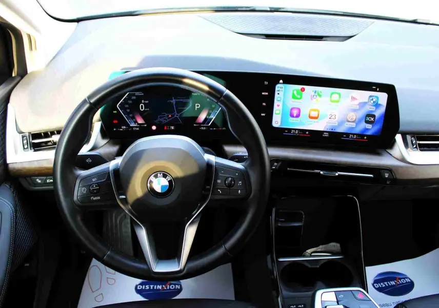 Vue intérieure centrée sur le volant cuir noir et l'écran tactile large du tableau de bord du BMW Série 2 Active Tourer gris Nardo.