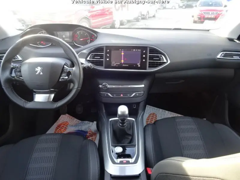 Intérieur noir de la Peugeot 308 SW 2018, vue frontale du poste de pilotage avec volant, écran tactile et levier de vitesse manuel.