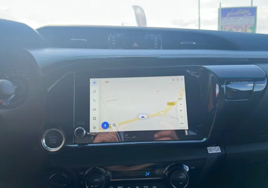 Tableau de bord du Toyota Hilux 4x4 Invincible 2025 avec écran tactile affichant un GPS, bouton start-stop et commandes climatisation.