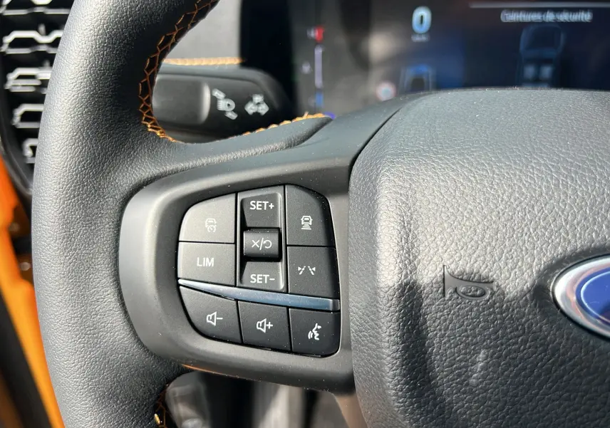 Gros plan sur le volant avec commandes multifonctions et surpiqûres orange du Ford Ranger Cyber orange 2025.