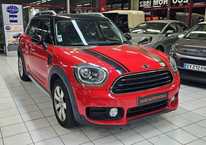 Vue 3/4 avant d'une MINI Cooper Countryman rouge avec bandes noires sur le capot, en showroom intérieur.