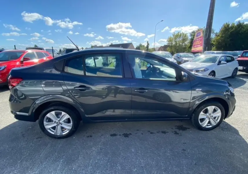 Vue latérale droite d'une Dacia Logan gris métallisé 2022 stationnée en extérieur sous un ciel bleu.